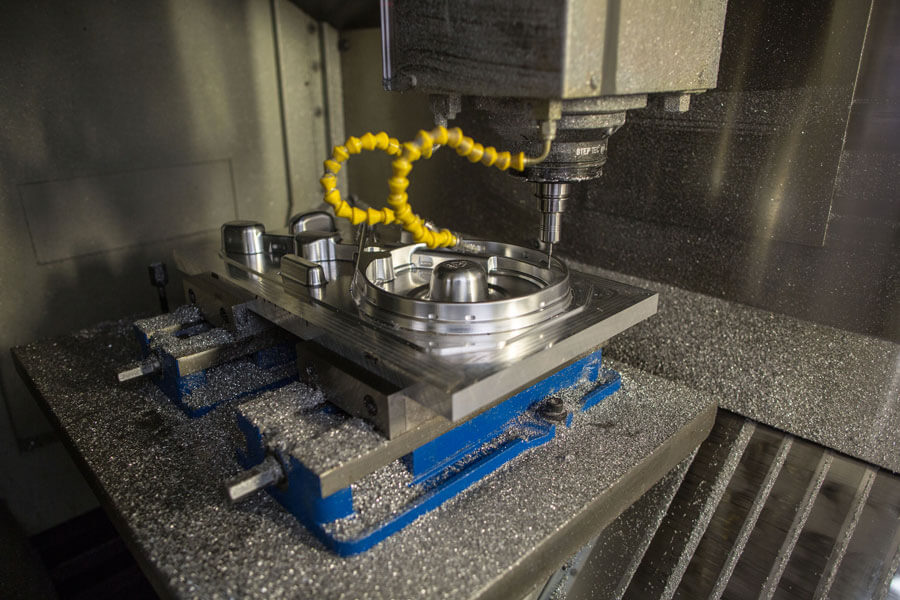 Two yellow coils branching off of a drill press shaping a metal component