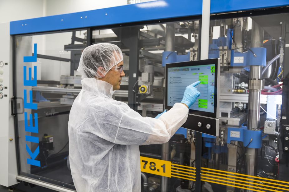 Thermoform engineer with a hair net and gloves touches a monitor