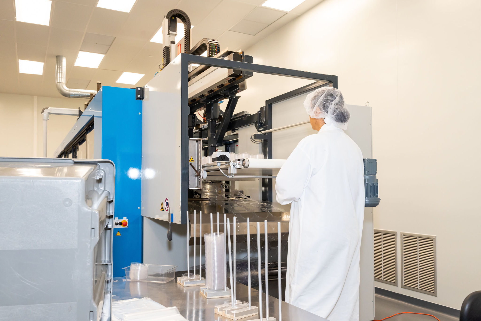 Tek Pak employee working on thin film production machine with a hairnet and white lab coat on.