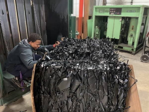 Large bin of black thermoforming tape with a man sifting through it from the side